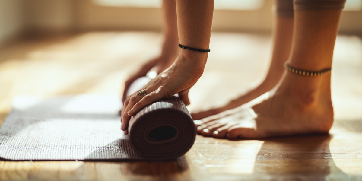 Close up of a woman's hands rolling up an exercise mat getting ready to do yoga. She works out on a floor mat in her home in the morning sunshine.