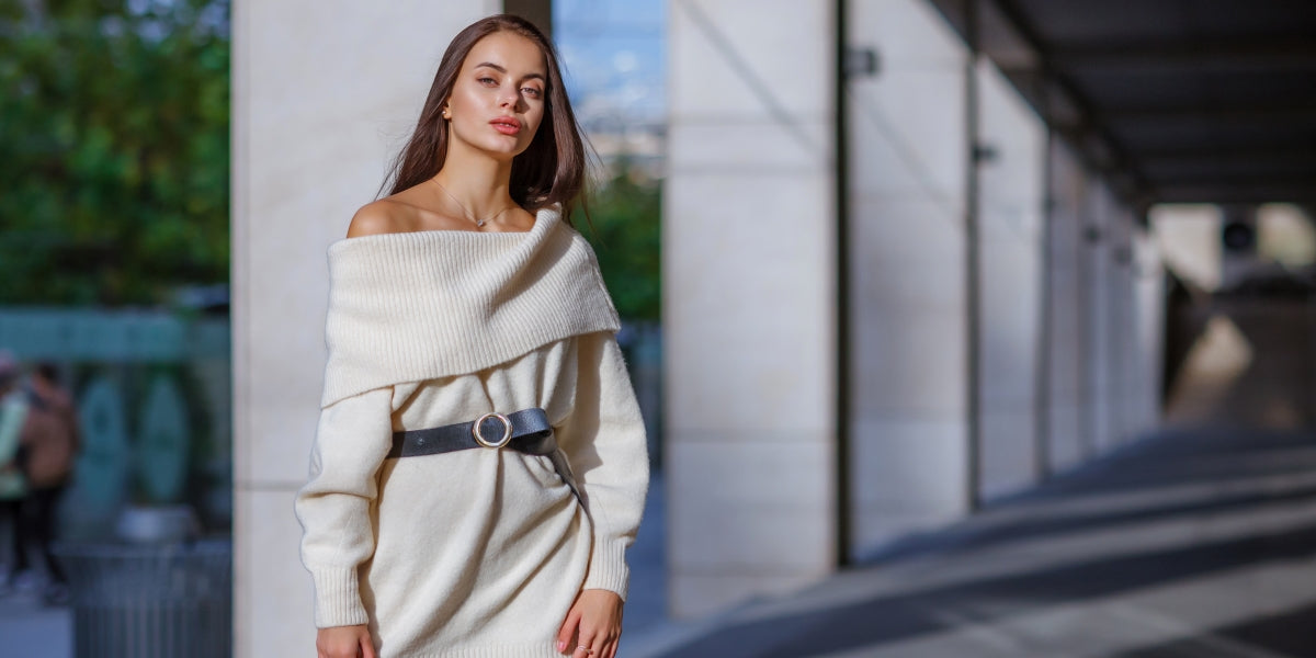 Fashion blogger outfit details. Fashionable woman wearing a white oversized sweater dress, holding a black trendy handbag. Detail of a perfect fall fashion outfit.