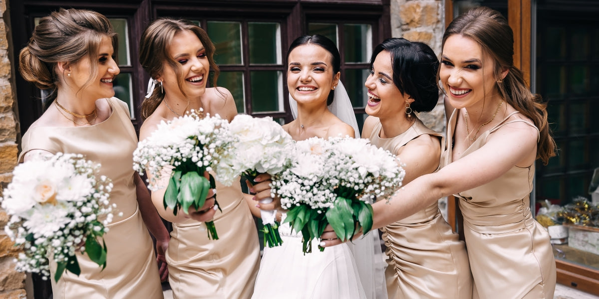 Group portrait of the bride and bridesmaids. A bride in a wedding dress and bridesmaids in golden dresses hold stylish bouquets of flowers on their wedding day.
