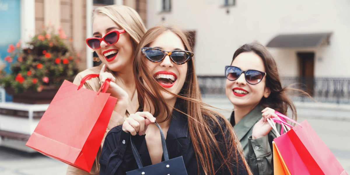 Stylish slim lady wearing trench coat and sunglasses walking in store near colorful shopping bags during shopping, concept of consumerism, sale, enriching life