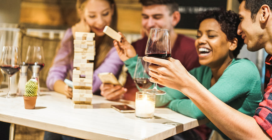 Young-friends-playing-board-games-at-home-Happy-people-having-fun-doing-party-in-living-room-house-at-evening-time-Fest-during-isolation-quarantine-Focus-on-close-up-hand-wine-glass
