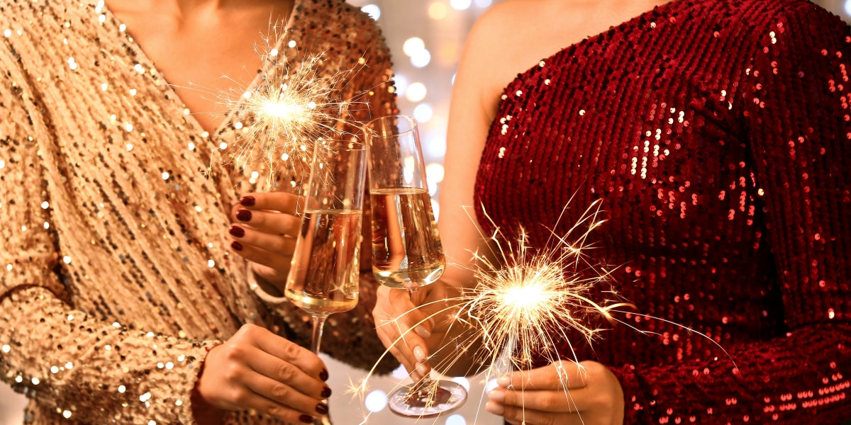 Young women in beautiful dresses with burning sparklers and glasses of champagne against Christmas lights