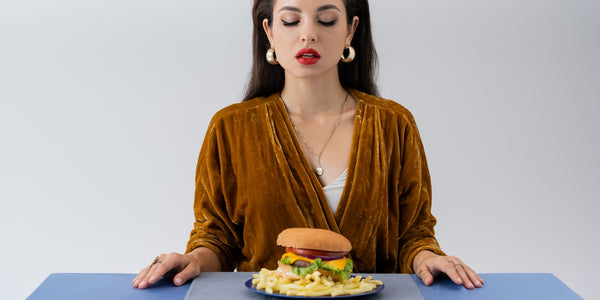 stylish woman in velvet dress looking at plate with french fries and burger on table isolated on grey