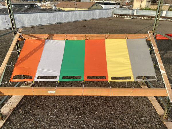 6 swatches of fabric suspended from racking on the roof of a building