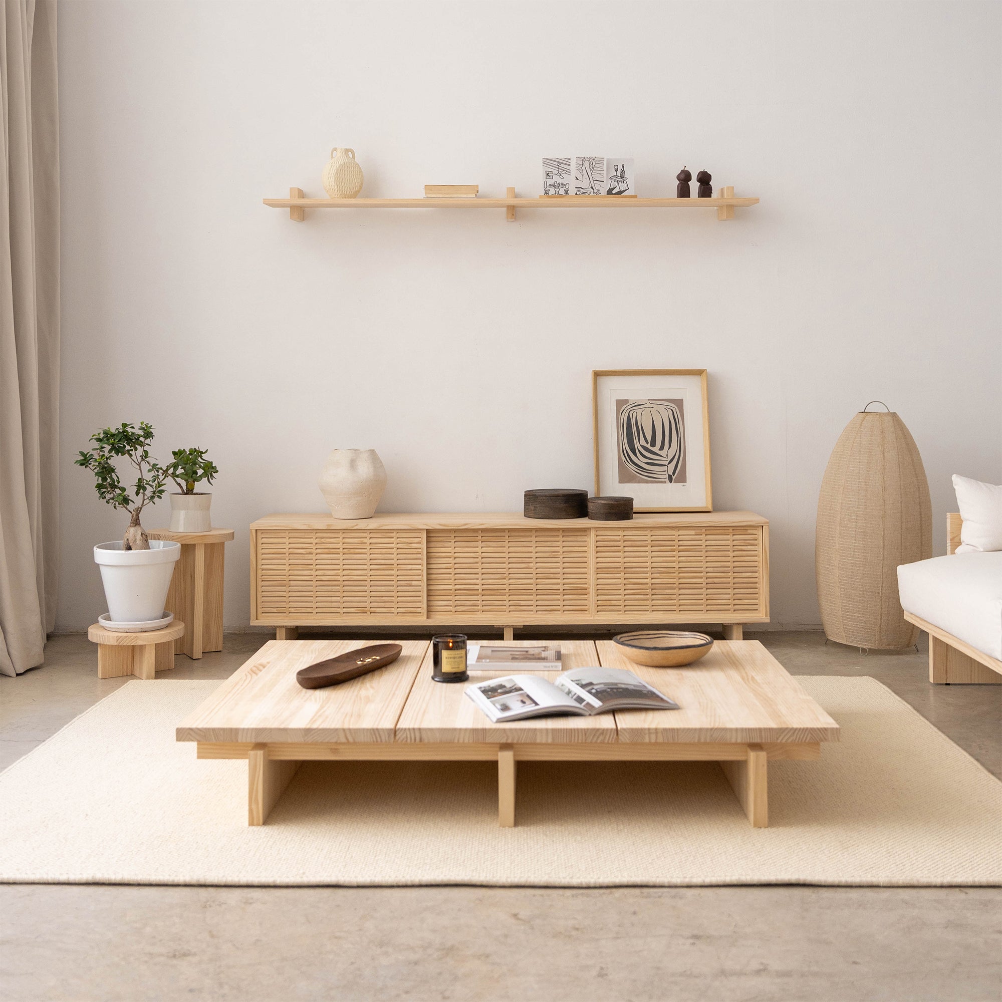 Neutral-toned living room with cream wool rug, low wooden coffee table, and natural wood TV stand against a white wall