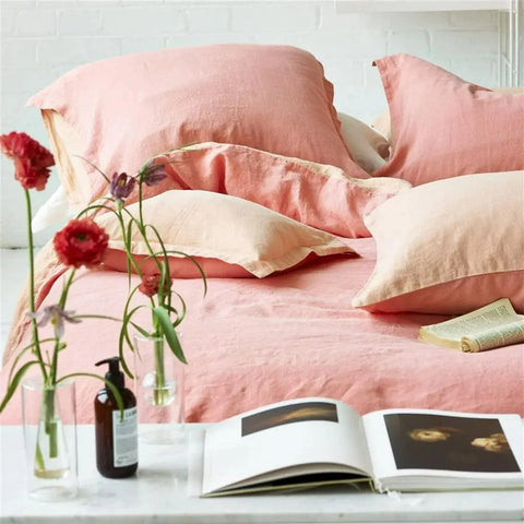 Peach duvet and pillow bedding set with small vases of flowers on a console