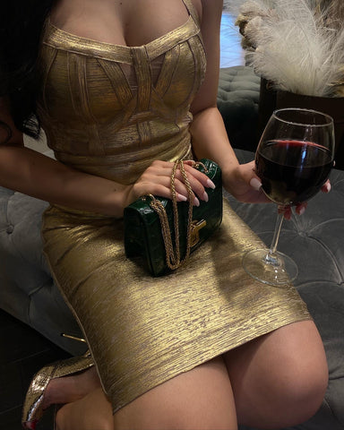 a woman in gold party dress holding a glass of wine and handbag on her lap