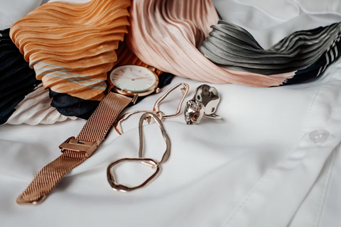 a watch scarf and bracelet placed on a white silk shirt