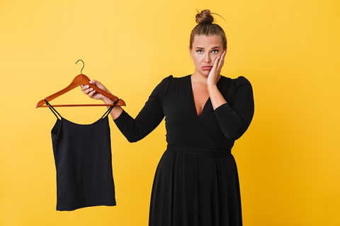 sad woman in a black dress holding a hanger in which a black top is hanging