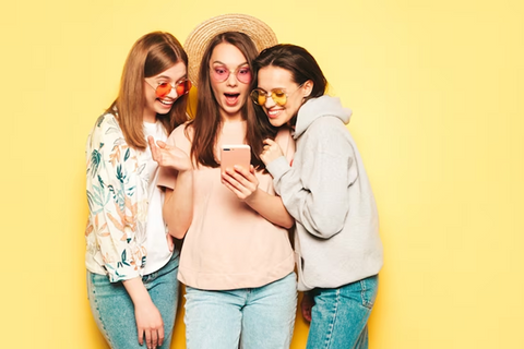 a group of 3 girls looking into a phone surprisingly