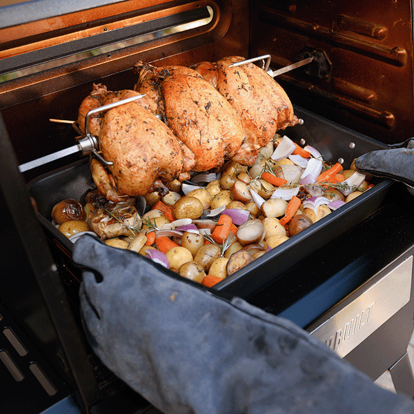 3 whole chickens roast on a Gravity Series rotisserie over a large pan of potatoes, carrots and onions