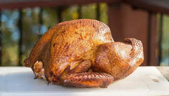 A whole smoked turkey rests on a white cutting board