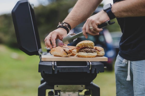 A man uses the left side shelf to hold buns for burgers and sausages as he takes them off the grill.