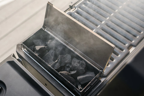 A Masterbuilt portable grill with the charcoal minihopper open to show smoking charcoal lumps