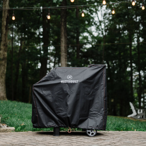 A Gravity Series Grill + Smoker sits outside on a patio. The grill is covered with a black Masterbuilt cover.