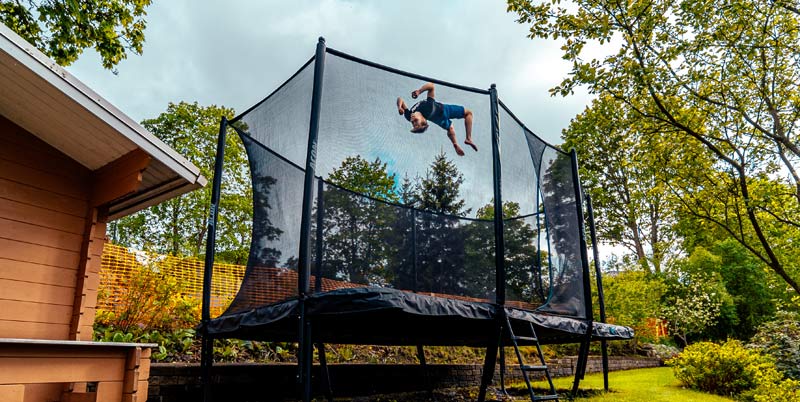 Trampoline in the backyard in a summer landscape, jumper doing a trick