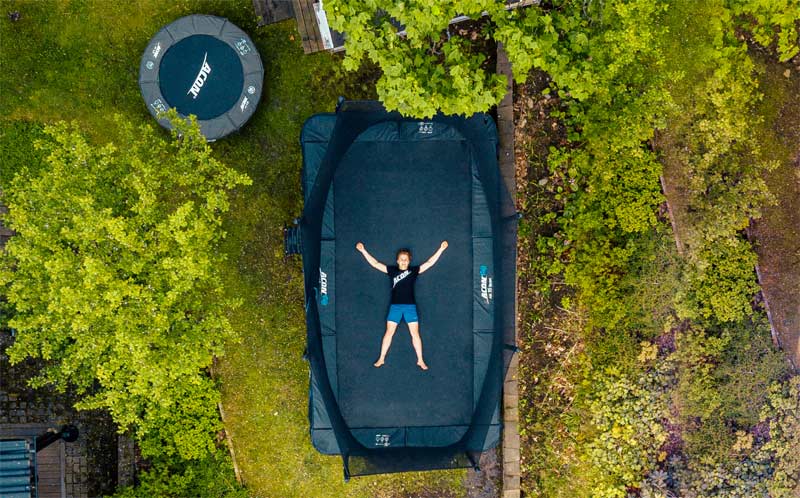 Yläkulmasta otettu kuva trampoliineista takapihalla. Poika makaa trampoliinin matolla