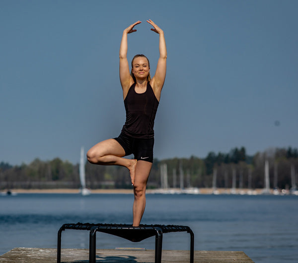 Joogaharjoittelua yhdellä jalalla tasapainoillein fitness trampoliinilla ulkona