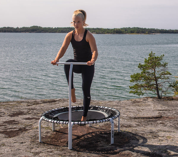 Nainen astuu kahvatangolla varustetun ACON fitness trampoliinin päälle