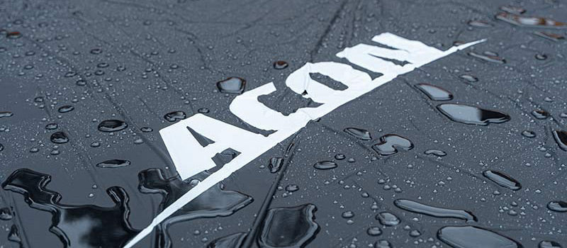 Droplets of water on an ACON weather cover. Image is a close-up and the brand logo is visible in white