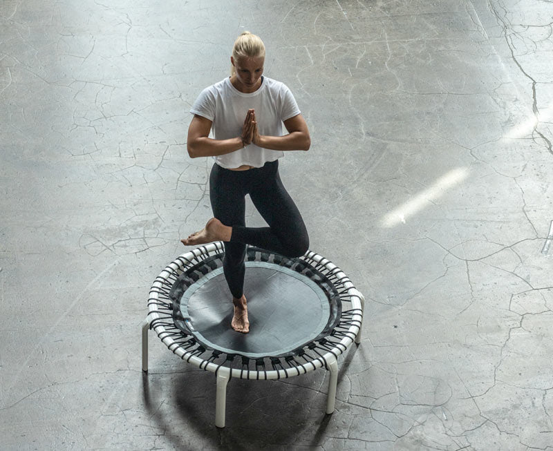 A woman making a yoga tree pose on a Acon FIT Trampoline