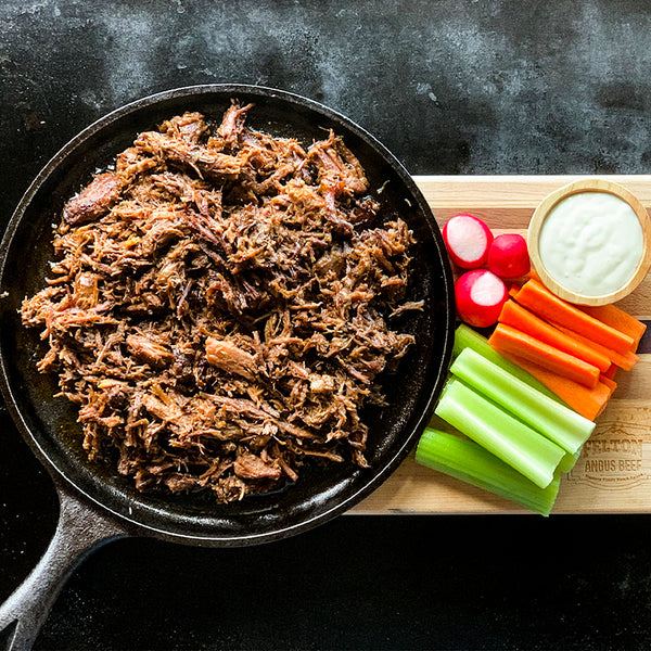 A pan of buffalo shredded beef beside carrots, celery, radishes and dip.