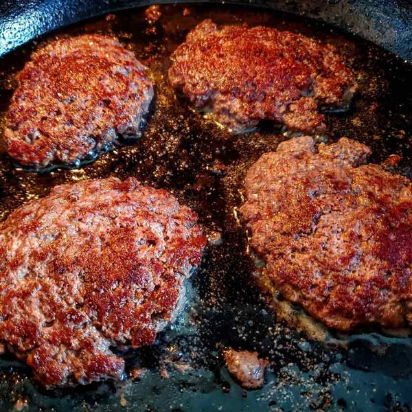 Smash burgers frying in a cast iron skillet