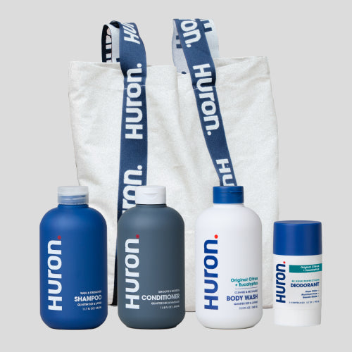 Set of Huron shampoo, conditioner, body wash, and deodorant in front of a branded tote bag.