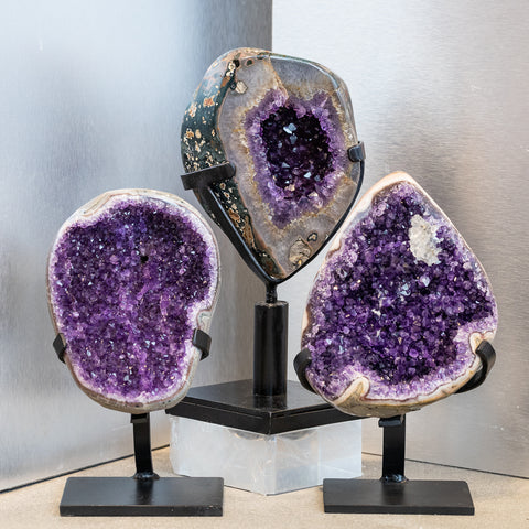 Three vibrant purple amethyst geode crystals on custom metal stands