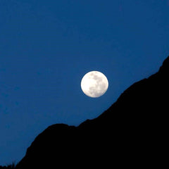 The moon with a dark blue sky and a diagonal mountain silhouette, representing the timeless method of moon bathing for metaphysical crystal cleansing.