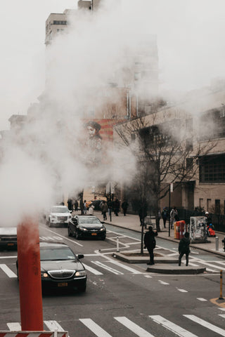 A busy street with cars and a steam pipe emitting vapor.