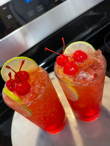 two shirley temple mocktails garnished with lime and maraschino cherries