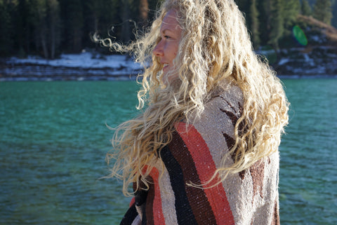 Blonde curly haired Girl wrapped in a mexican woven blanket by a mountain lake