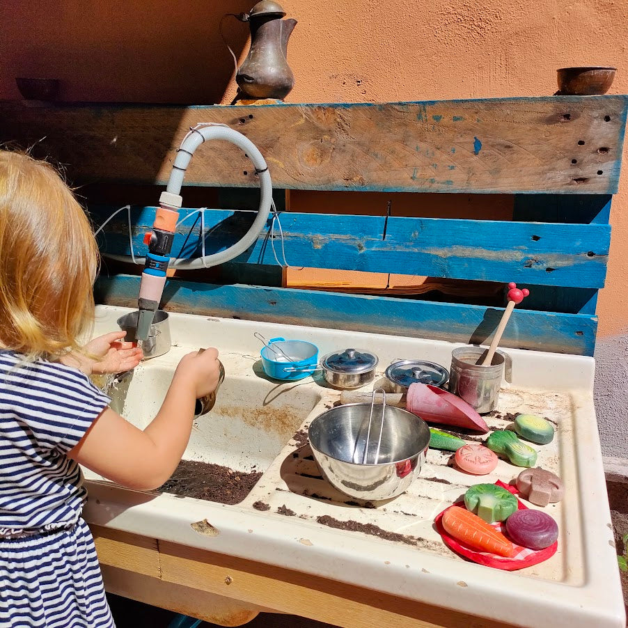 Bambina che gioca con il fango in una mud kitchen con pietre sensoriali di Yellow Door