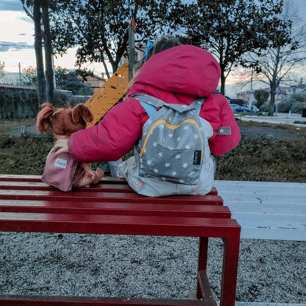 Bambina con la sua bambola Minikane, di spalle, con lo zaino abbinato. 