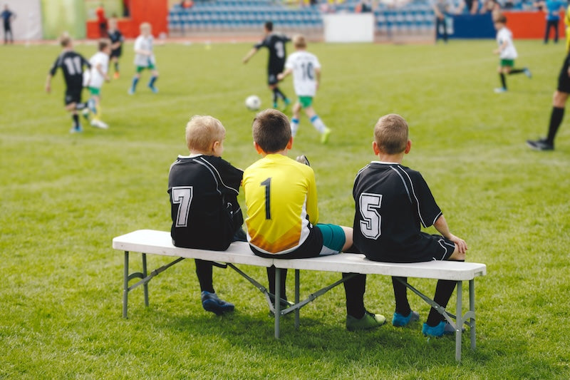 3 boys sitting on the bench of a soccer field