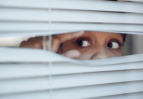 a person uses their fingers to open the blinds and peek out the window