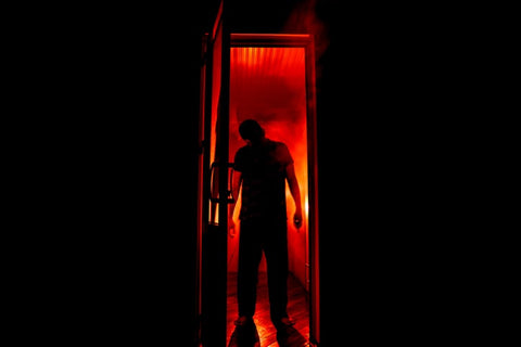 outline of a person standing in a doorway backed by red light and smoke