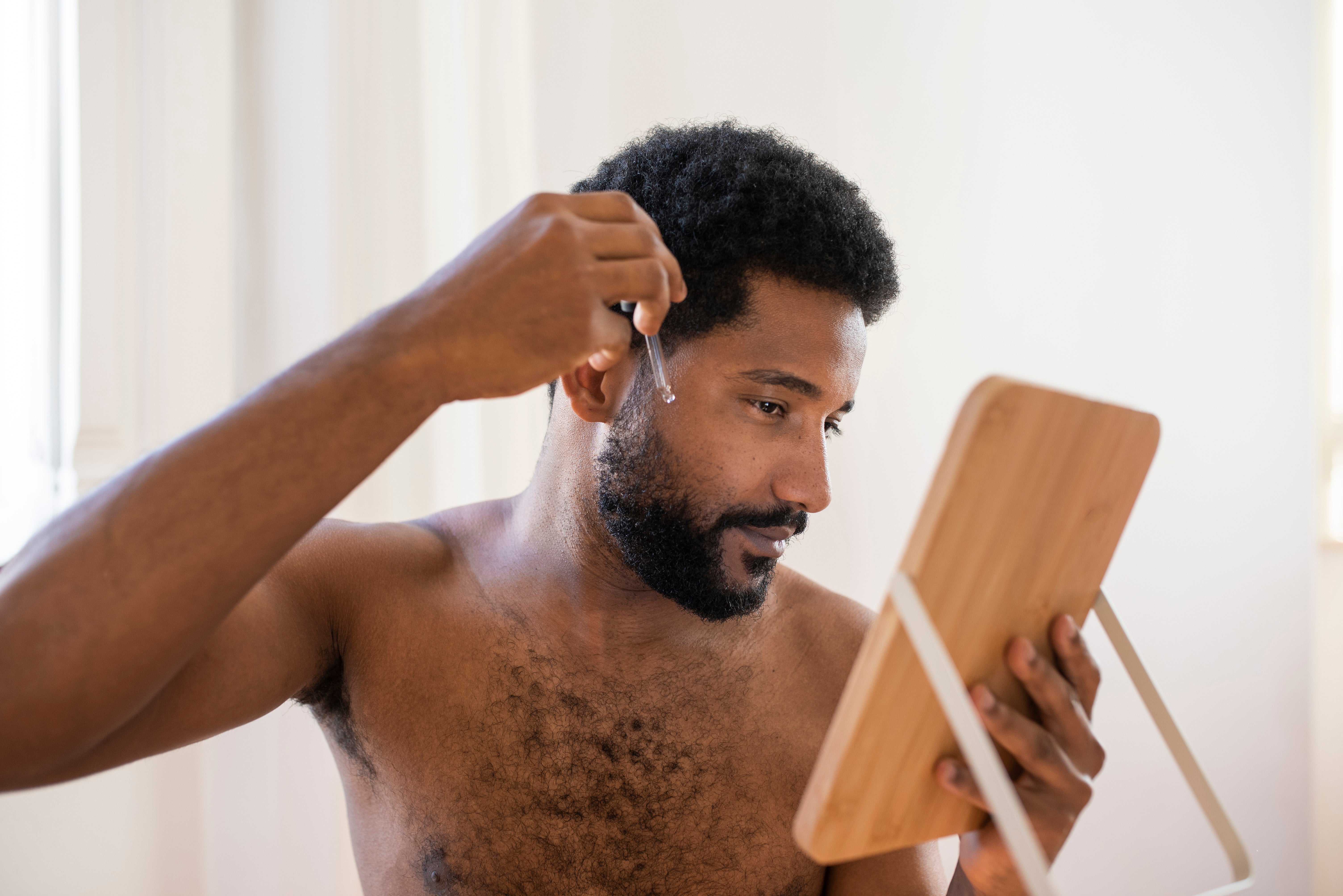 Man holding a mirror while using beard oil on facial hair