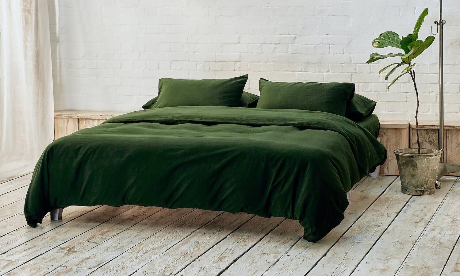 dark green duvet cover, two pillowcases, and bottom sheet on double bed in apartment with plant and wooden flooring