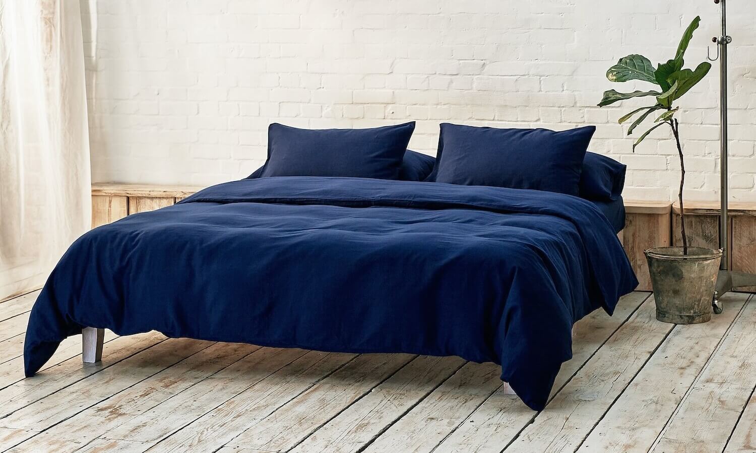 navy blue duvet cover, two pillowcases, and bottom sheet on double bed in apartment with plant and wooden flooring