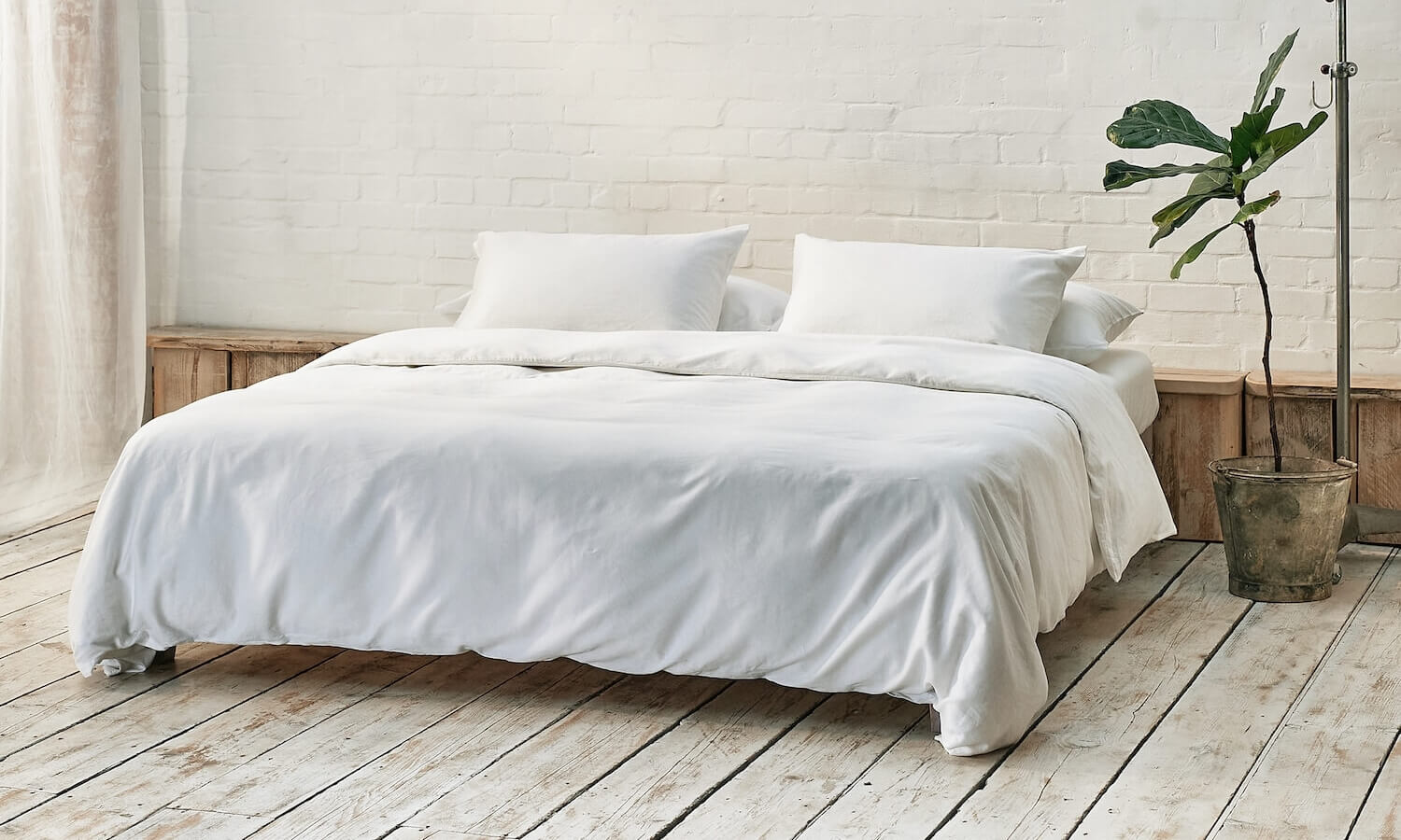 white duvet cover, two pillowcases, and bottom sheet on double bed in apartment with plant and wooden flooring
