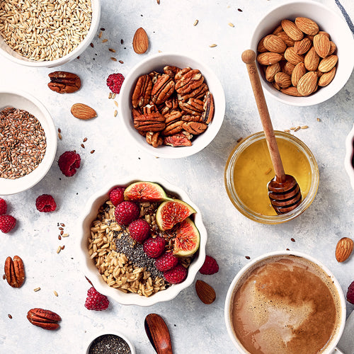 bowls of different healthy snacks such as nuts, honey, and fruits on a white background