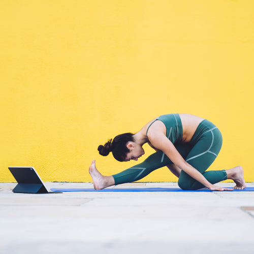 a woman is stretching in front of a yellow wall