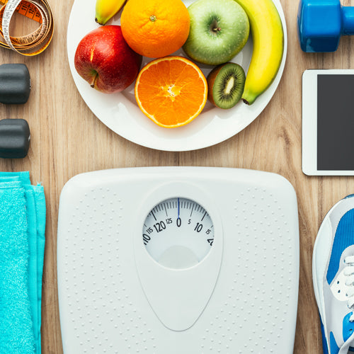 a plate of fruits and a scale with dumbbells on a wood table