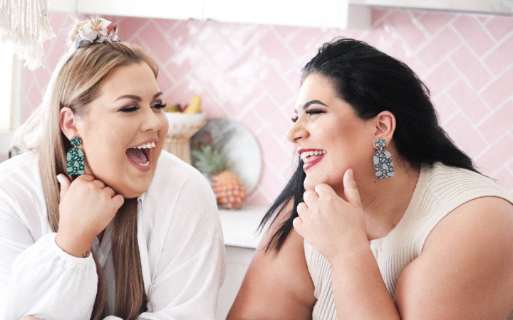 Two women wearing statement earrings laughing together.