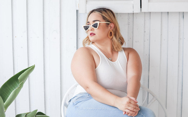 Woman sitting down wearing a white top, sunglasses and earrings looking confident.