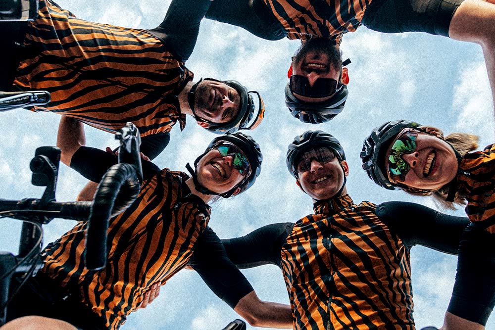 Imagen tomada desde abajo en la que cinco componentes de la grupeta Makeba Cycling se abrazan sonrientes. 