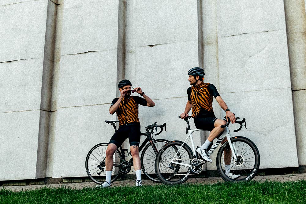 Deux cyclistes de l'équipe, appuyés sur leur vélo et portant leur équipement. custom de GobikIls discutent et se préparent au départ. 