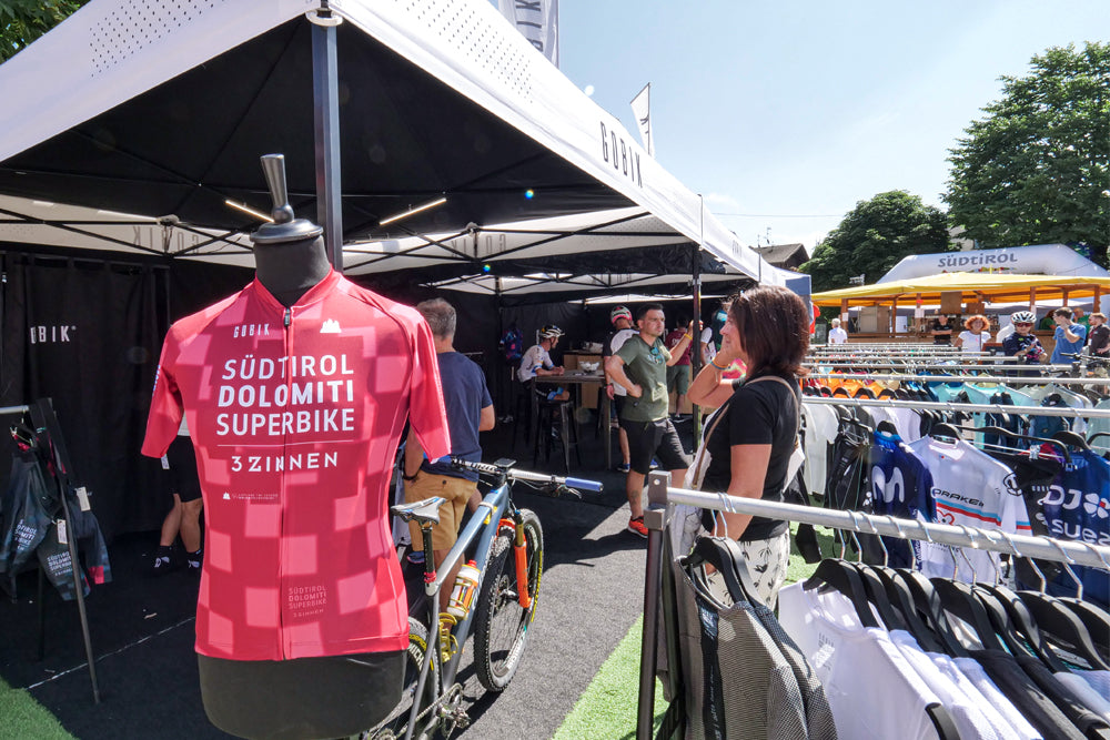 Exposición del maillot de Gobik diseñado para la prueba en el stand de la marca tras su presentación. El diseño incluye el nombre de la prueba en letras blancas sobre un fondo de cuadros en tonos rosas y burdeos.